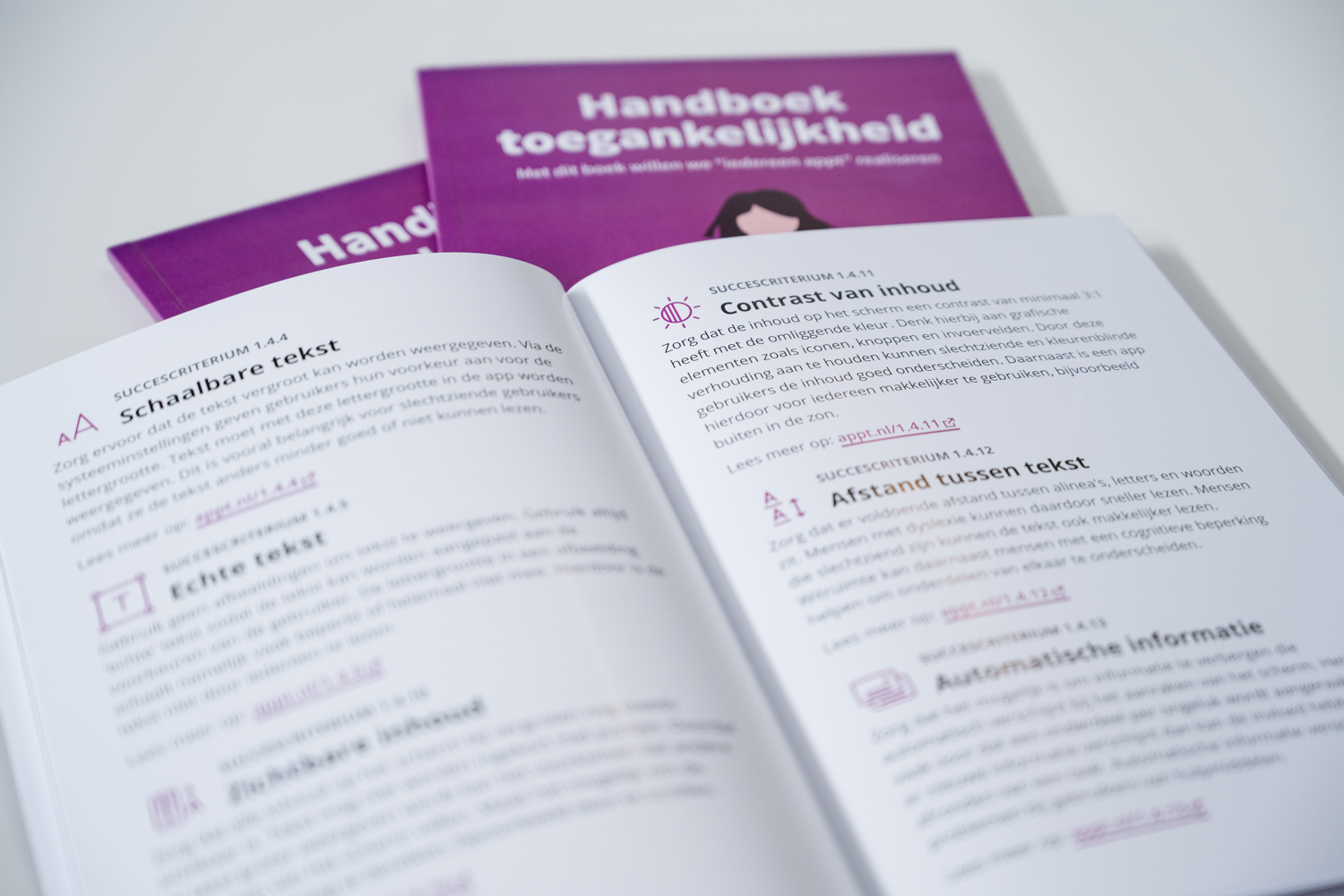 Multiple handbooks are laying on a table, one is open and shows content about the accessibility guidelines